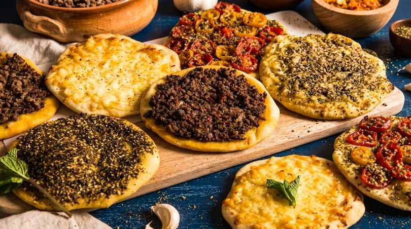 Assortment of Middle Eastern flatbreads with various toppings like meat, cheese, za'atar, and tomatoes.
