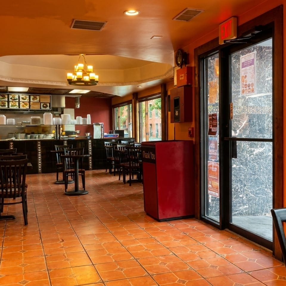 Empty restaurant interior with orange and red walls, tiled floor, and dark wooden tables and chairs.