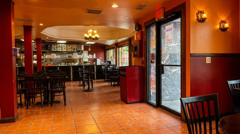 Empty restaurant interior with orange and red walls, tiled floor, and dark wooden tables and chairs.