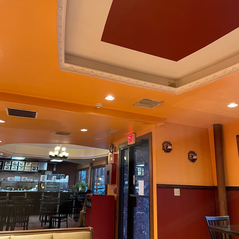 Interior of a restaurant with orange and red walls, booths, tables, and a counter area.