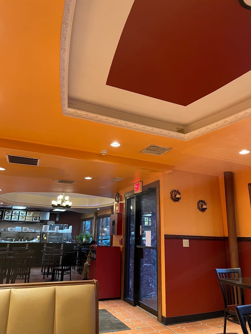 Interior of a restaurant with orange and red walls, booths, tables, and a counter area.