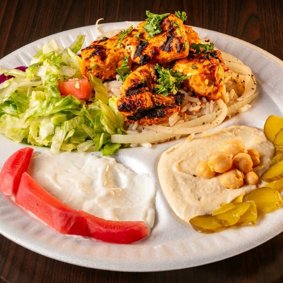 Grilled chicken skewers with rice, salad, hummus, pickles, and white sauce on a plate.