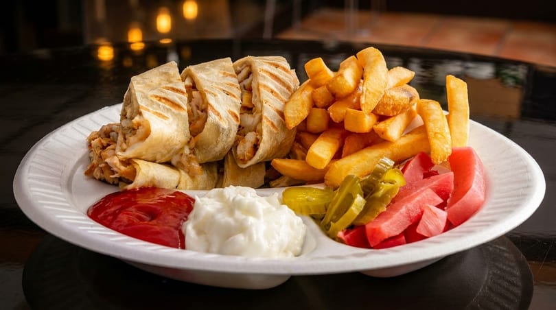 Chicken shawarma wraps, french fries, pickles, and sauces on a white plate.