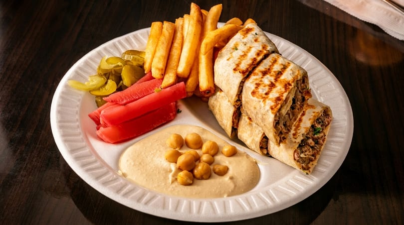 Shawarma wraps, french fries, hummus with chickpeas, and pickled vegetables on a white plate.
