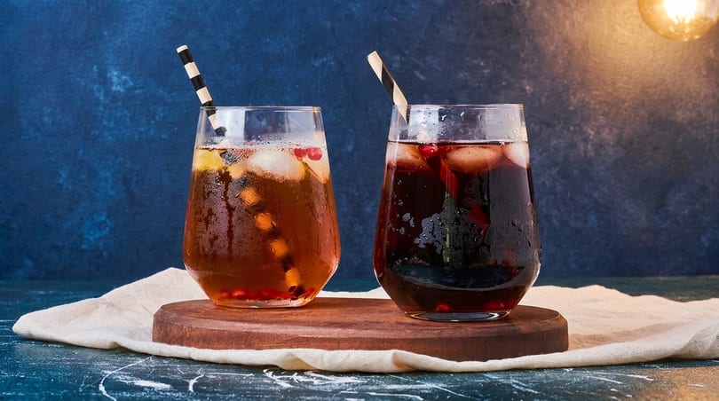 Two glasses of iced tea, one light brown and one dark red, with pomegranate seeds and straws.