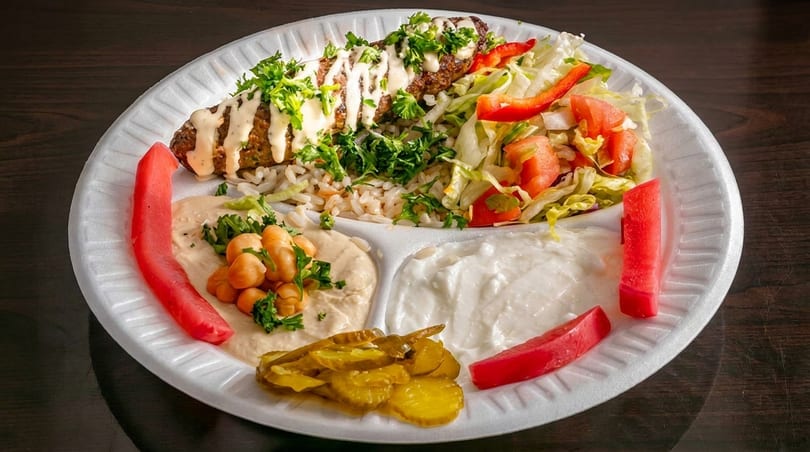 Kebab plate with rice, salad, hummus, yogurt, pickles, and pickled turnips on a white plate.